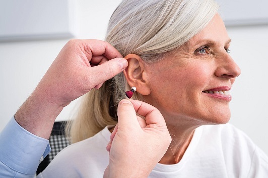 Ältere Frau bekommt ein modernes Hörgerät ins Ohr eingesetzt, Hörakustik Beratung.